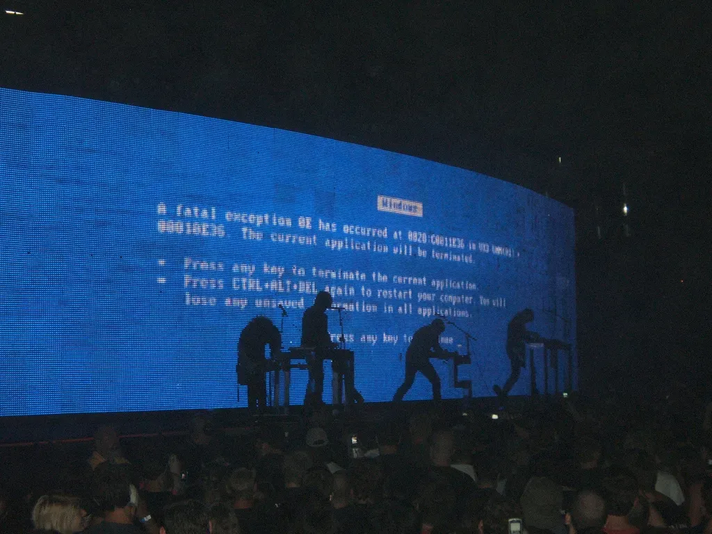 A band playing in front of a video wall with a Windows bluescreen of death